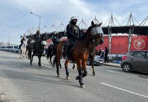 Policjanci s strażnicy miejscy jadą konno ulicą przy stadionie.
