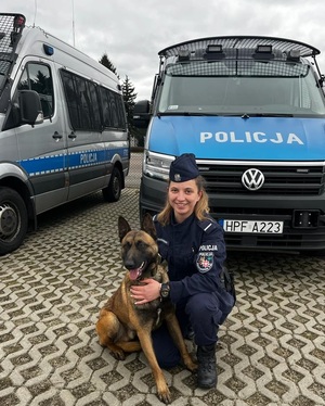 Przewodnik i jego pies służbowy na tle radiowozu.