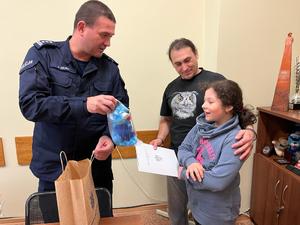 Inspektor Dariusz Dziurka wręcza córce wyróżnionego mężczyzny maskotkę Kota Prewencjusza.