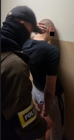 Policjant zakłada kajdanki na ręce zatrzymanego.
