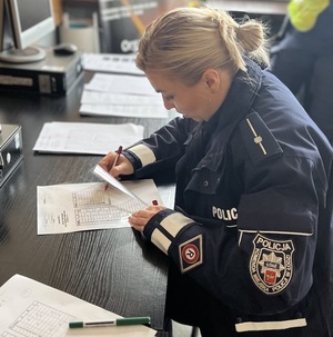 Policjanta sprawdza testy z wiedzy o przepisach ruchu drogowego.