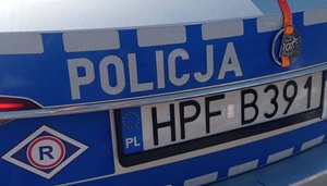 Tył radiowozu policyjnego , na nim napis POLICJA, wyróżnik z literą R ruchu drogowego oraz powieszony na nim medal maratonu.