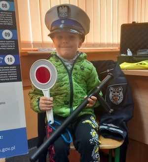 Chłopczyk siedzi na krześle i pozuje w czapce policjanta ruchu drogowego z tarczą do zatrzymywania w dłoni.