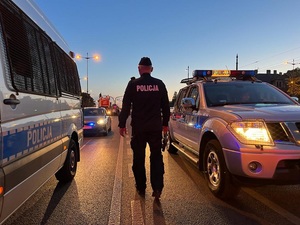 Policjant na tle radiowozów.