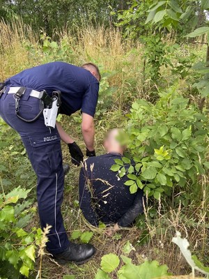 Policjant trzyma mężczyznę, który ma założone kajdanki na ręce.