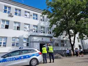 Policjantka i funkcjonariusz Straży Miejskiej w Łodzi na tle szkoły, obok nich radiowóz policyjny i dzieci.