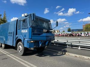Radiowóz policyjny a w tle kibice Cracovii wysiadają z pociągu na dworcu Łódź Niciarniana.