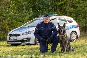 Policjant klęczy obok pies policyjny.