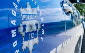 Odznaka policyjna na drzwiach radiowozu z napisem pomagamy i chronimy oraz policja i numerem alarmowym 112.