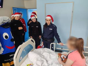 Policjanci rozmawiają z dziewczynką siedzącą w łóżku.