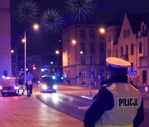 Policjant obserwujący ruch uliczny, na niebie fajerwerki.