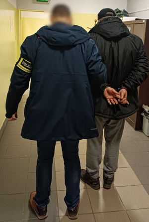 Policjant prowadzi korytarzem zatrzymanego.