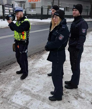 Goście obserwują jak policjant ruchu drogowego mierzy prędkość nadjeżdżających pojazdów.