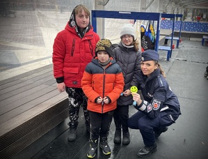 Policjantka trzyma odblask obok stoją dzieci.