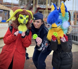 Policjantka i dziećmi z założonymi maskami. Wszyscy trzymają odblaski.
