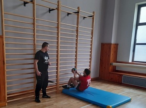 Uczestnik konkursu w trakcie pokonywania toru przeszkód wykonuje na materacu skłony z piłką lekarską.