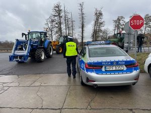 Funkcjonariusz Wydziału Ruchu Drogowego łódzkiej komendy przy radiowozie w trakcie zabezpieczenia protestu rolników.