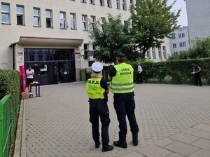 Umundurowany policjant i strażnik miejski w trakcji kontroli bezpieczeństwa przed szkołą.