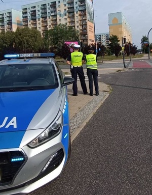 Umundurowany policjant i strażnik miejski w trakcji kontroli bezpieczeństwa przed szkołą.