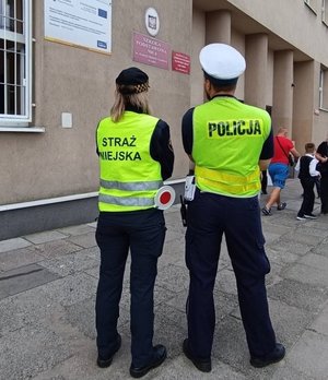 Umundurowany policjant i strażnik miejski w trakcji kontroli bezpieczeństwa przed szkołą.