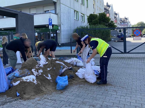 Policjantka napełnia worki z piachem wraz z mieszkańcami.