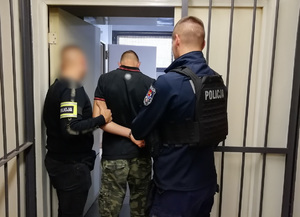 Policjanci trzymają zatrzymanego mężczyznę.