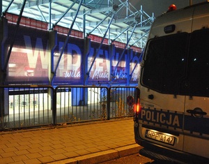 Oznakowany radiowóz policyjny na tle stadionu.