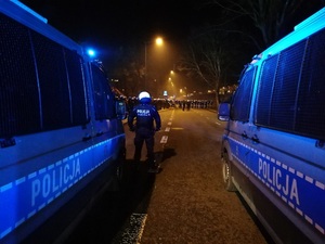 Policjant stoi między radiowozami.