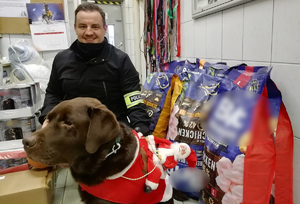 Organizator zbiórki - sierżant sztabowy Łukasz Sobala wraz ze swoim pomocnikiem - labradorem Maciejem na tle zebranych darów.