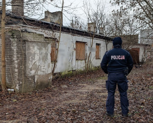 Umundurowany policjant stojący przed pustostanem.