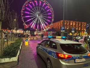 Radiowóz policyjny stoi na tle młyńskiego koła i centrum handlowego.