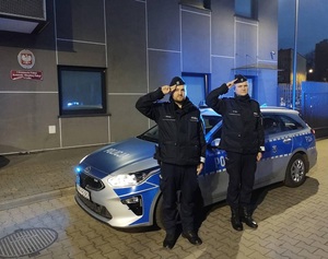 Policjanci stoją przed radiowozem i oddają hołd.