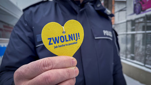 Umundurowany policjant trzyma serduszko z napisem &quot;Zwolnij! Jak kocha to poczeka.&quot;