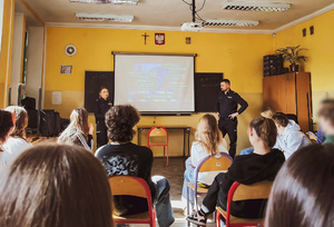 Umundurowani policjanci, w klasie, na spotkaniu z uczniami.