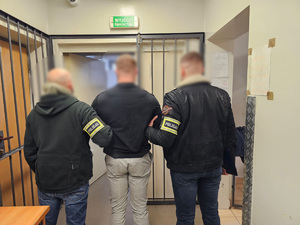 Dwóch policjantów trzyma za ręce zatrzymanego mężczyznę.