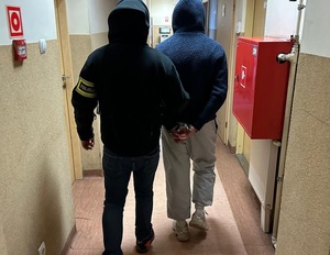 Policjant prowadzi zatrzymanego mężczyznę.