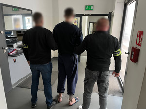Policjanci z zatrzymanym mężczyzną, który ma założone kajdanki zespolone.