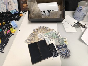 Zabezpieczone przez policjantów pieniądze, elektronika i narkotyki, leżą na stole, a przy nich naszywka z logo Wydziału Patrolowo - Wywiadowczego.