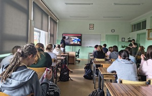 Umundurowany policjant, w klasie, w trakcie zajęć z młodzieżą.