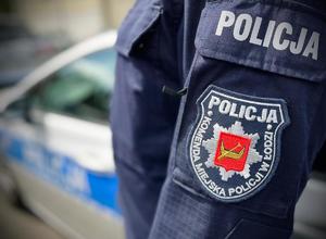 Naszywka Komendy Miejskiej Policji w Łodzi na rękawie munduru, w tle radiowóz policyjny.