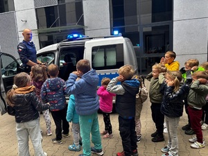 Policjant prezentuje przedszkolakom radiowóz policyjny.