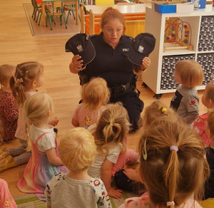 Policjantka prezentuje dzieciom czapki policyjne.
