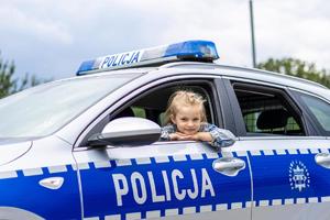 Dziewczynka wygląda przez okno oznakowanego radiowozu policyjnego.