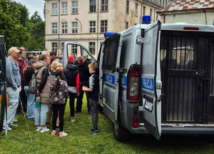 Policjanci stoją przy radiowozie policyjnym i rozmawiają, na pikniku, z uczestnikami zabawy.