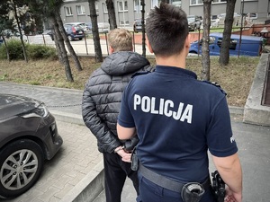 Policjant prowadzi zatrzymanego mężczyznę.