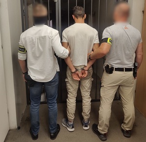 Policjanci trzymają mężczyznę, który ma kajdanki założone na ręce z tyłu.