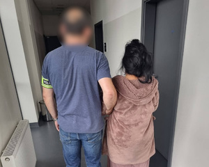 Policjant prowadzi zatrzymaną kobietę.