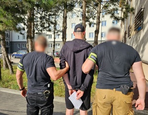 Policjanci trzymają mężczyznę, który ma założone kajdanki na ręce z tyłu.