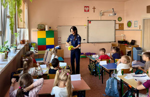 Policjantka rozdaje dzieciom elementy odblaskowe.