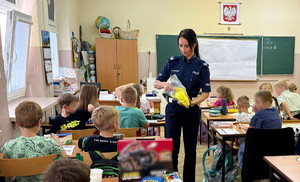 Policjantka rozdaje dzieciom elementy odblaskowe.